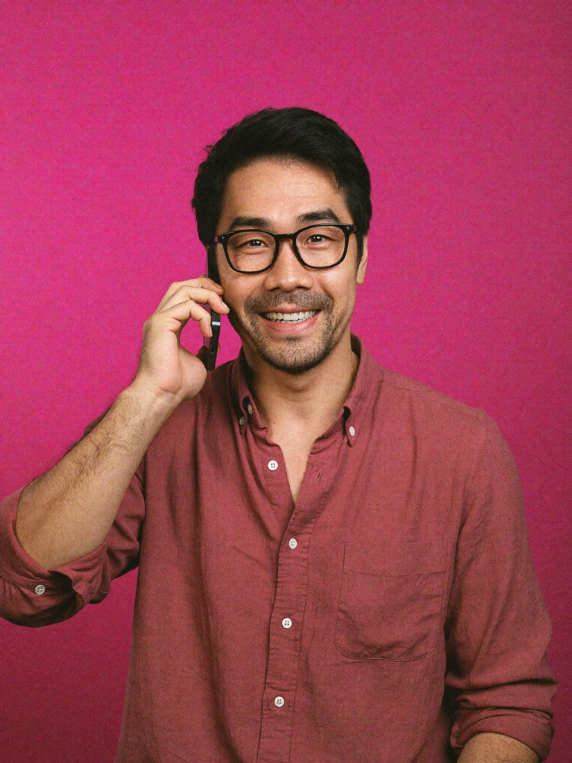 Ly on the phone, smiling, against a pink wall