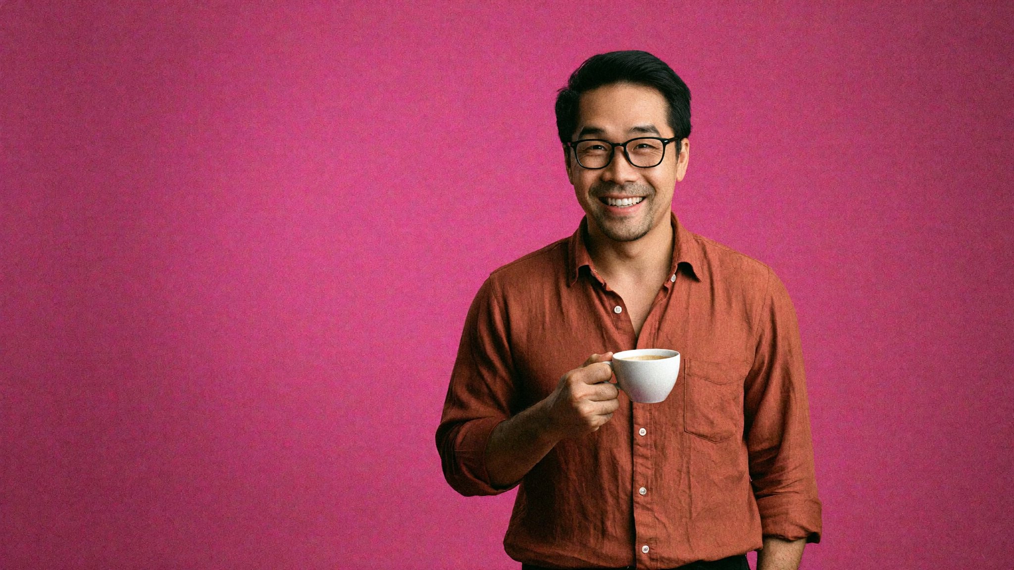Ly in glasses and a rust shirt, smiling, holding a cup of coffee